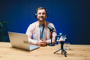 Man podcaster influencer blogger smiling while broadcasting his live audio podcast in studio using headphones. Male radio host making podcast or interview photo