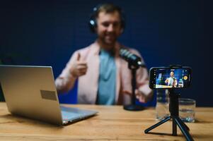Man podcaster influencer blogger smiling while broadcasting his live audio podcast in studio using headphones. Male radio host making podcast or interview photo