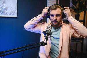 Man podcaster influencer blogger smiling while broadcasting his live audio podcast in studio using headphones. Male radio host making podcast or interview photo