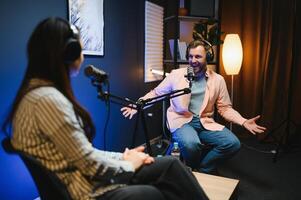Female podcaster in headphones interviewing man guest using microphone, smiling, recording and broadcasting audio podcast in studio. Content creator, blogging photo