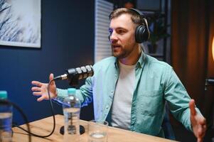 Man podcaster influencer blogger smiling while broadcasting his live audio podcast in studio using headphones. Male radio host making podcast or interview photo