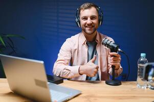 Man podcaster influencer blogger smiling while broadcasting his live audio podcast in studio using headphones. Male radio host making podcast or interview photo