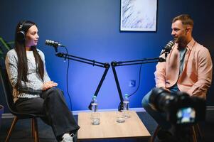 Female podcaster in headphones interviewing man guest using microphone, smiling, recording and broadcasting audio podcast in studio. Content creator, blogging photo