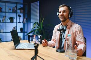 Man podcaster influencer blogger smiling while broadcasting his live audio podcast in studio using headphones. Male radio host making podcast or interview photo