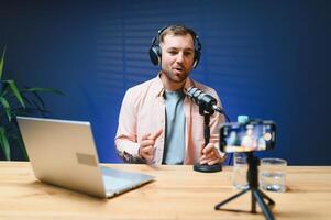 Man podcaster influencer blogger smiling while broadcasting his live audio podcast in studio using headphones. Male radio host making podcast or interview photo