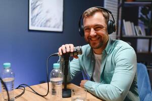 Man podcaster influencer blogger smiling while broadcasting his live audio podcast in studio using headphones. Male radio host making podcast or interview photo