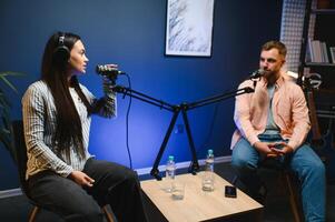 Female podcaster in headphones interviewing man guest using microphone, smiling, recording and broadcasting audio podcast in studio. Content creator, blogging photo