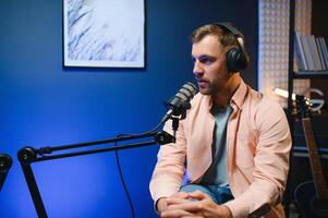 Man podcaster influencer blogger smiling while broadcasting his live audio podcast in studio using headphones. Male radio host making podcast or interview photo