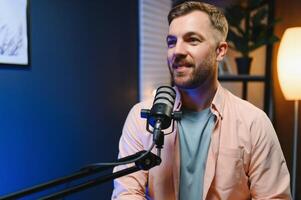 Man podcaster influencer blogger smiling while broadcasting his live audio podcast in studio using headphones. Male radio host making podcast or interview photo