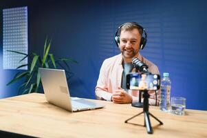 Man podcaster influencer blogger smiling while broadcasting his live audio podcast in studio using headphones. Male radio host making podcast or interview photo
