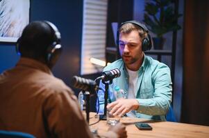 Show host and guest meeting to stream podcast episode together, creating online content with live broadcast discussion. Vlogger talking to man using professional equipment to record chat photo