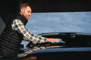 A man wipes his car with a microfiber towel after washing it at a car wash photo