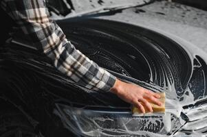 Man worker with a sponge washes a car with foam. Car wash and car care photo