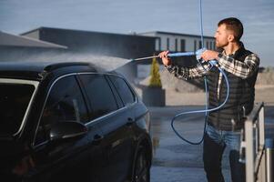 A man washes his car at a self service car wash using a hose with pressurized water. photo