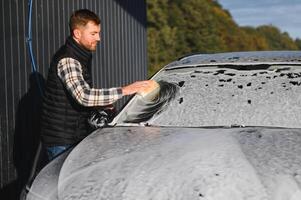 Man worker with a sponge washes a car with foam. Car wash and car care photo