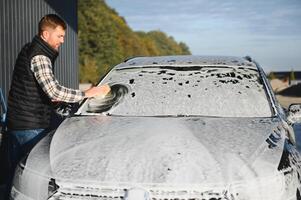 A man washes a car with a sponge at a self-service car wash photo