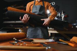 Tailor cobbler hold different rolls natural brown leather, working in workshop. Concept banner Industrial professional craftsman master photo