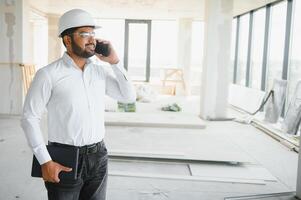 Indian construction site manager standing wearing helmet, thinking at construction site. Portrait of mixed race manual worker or architect photo