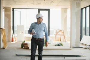Portrait of an architect builder studying layout plan of the rooms, civil engineer working with documents on construction site photo