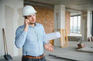 Portrait of an architect builder studying layout plan of the rooms, civil engineer working with documents on construction site photo