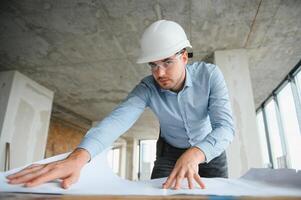 Portrait of an architect builder studying layout plan of the rooms, civil engineer working with documents on construction site photo