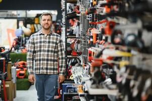 Confident smiling salesman on foreground in power tools store. Guy is ready to help clients on background photo