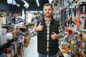 Confident smiling salesman on foreground in power tools store. Guy is ready to help clients on background photo