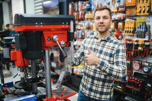 Confident smiling salesman on foreground in power tools store. Guy is ready to help clients on background photo