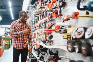African americam man buying modern electric drill while standing in tool. Hardware construction site objects concept photo