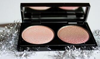 A palette of two eyeshadow shades light tan, soft peach with silver tinsel scattered delicately around the palette photo