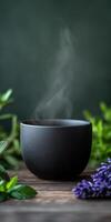 Hot drink steaming in a black cup surrounded by herbs photo