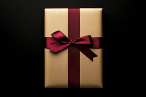 Festive gold gift box with maroon ribbon on black background photo