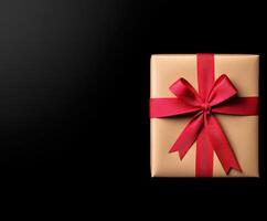 Gift wrapped in brown paper with red ribbon on black background photo