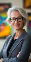 Confident woman with gray hair and glasses poses indoors photo