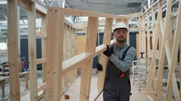 Carpenter engineer in uniform walks with frame through unfinished prefabricated modular house in construction site video