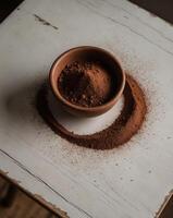 Top view of a bowl filled with cocoa powder placed on a wooden table surface with scattered cocoa powder around photo