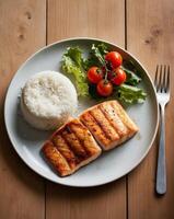 Grilled fish fillet served with rice and fresh salad on a wooden table photo