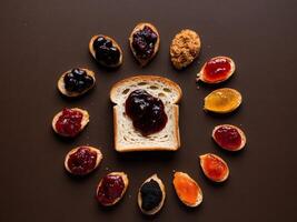 Toasted bread slice with assorted fruit preserves and jams spread on a dark background surface. photo