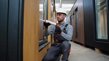 A worker is applying polyurethane foam to fill gap between sash and window frame in prefabricated modular house video