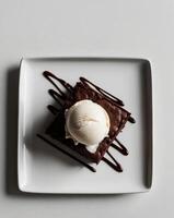 Overhead view artisanal dessert platter square white plates chocolate brownie vanilla ice cream scoop chocolate sauce drizzle. photo