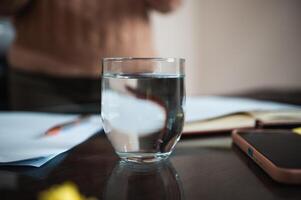 Glass of water on a desk with papers and notebook in background photo