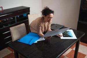 Woman reviewing photographs on a table with blue folder and laptop photo