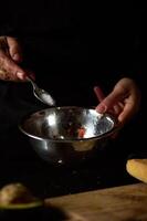 Hand adding salt to metal bowl during cooking preparation in dim lighting photo
