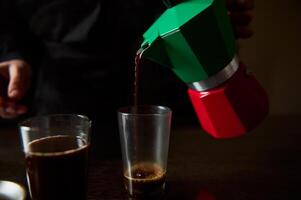 Pouring freshly brewed coffee from a colorful moka pot into a glass photo