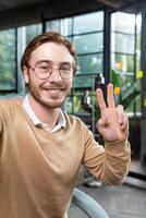 Close-up photo. Portrait of professional smart male programmer hacker taking selfie with hand, showing victory gesture with fingers. Smiles into the phone camera. photo