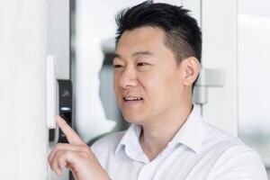 Close-up photo. Portrait of a young handsome Asian man, calling the intercom of the house, pressing the button, waiting for the door to open. photo