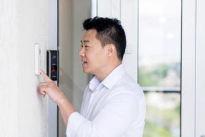 Close-up photo. Portrait of a young handsome Asian man, calling the intercom of the house, pressing the button, waiting for the door to open. photo