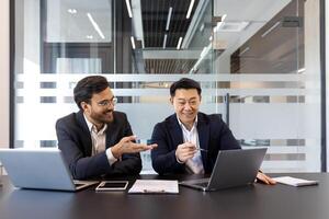 Two businessmen are engaged in a collaborative meeting in a contemporary office setting. They are using laptops and documents, creating a dynamic and professional atmosphere for business planning photo