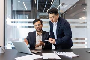 Two professionals in modern office collaborating on project, using laptop and smartphone. Discussing data for successful business outcomes and effective team collaboration. photo