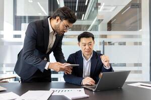 Two professionals collaborate in modern office using laptop and smartphone, emphasizing teamwork, technology, productivity. Engaged managers discussing ideas, showcasing business strategy photo